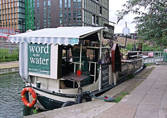 Floating bookstore moored along a canal, showcasing a cozy and magical library experience on the water.