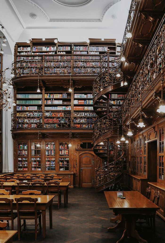 Grandioso interno di biblioteca con scaffali in legno, scala a chiocciola e accoglienti tavoli da lettura pieni di libri da tutto il mondo. Grandioso interno di biblioteca con scaffali in legno, scala a chiocciola e accoglienti tavoli da lettura pieni di libri da tutto il mondo.