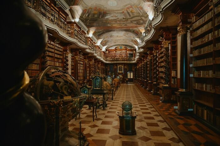 Interior grandioso de uma biblioteca com globos antigos, colunas ornamentadas e fileiras de livros antigos em prateleiras de madeira. Interior grandioso de uma biblioteca com globos antigos, colunas ornamentadas e fileiras de livros antigos em prateleiras de madeira.