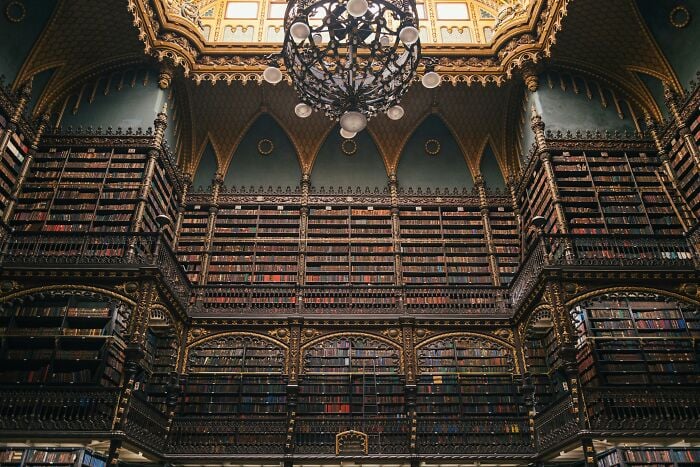 Ornate grandiose library interior with towering bookshelves and intricate gold detailing under a decorative chandelier. Ornate grandiose library interior with towering bookshelves and intricate gold detailing under a decorative chandelier.
