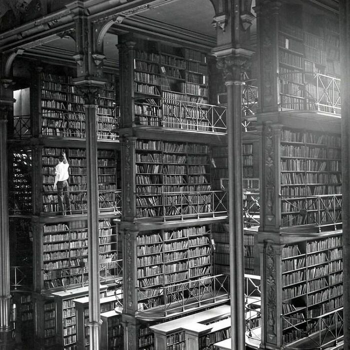 Grandiose library interior with towering bookshelves, multiple balconies, and a person reaching for a book in a magical setting. Grandiose library interior with towering bookshelves, multiple balconies, and a person reaching for a book in a magical setting.