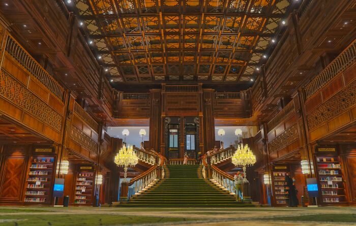 Grandiose library interior with a grand staircase, wooden ornate walls, and shelves filled with books in a magical setting. Grandiose library interior with a grand staircase, wooden ornate walls, and shelves filled with books in a magical setting.